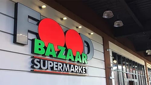A modern storefront sign for Food Bazaar Supermarket. The word FOOD is large, with red circles as the Os, and BAZAAR and SUPERMARKET are below in green and white letters.