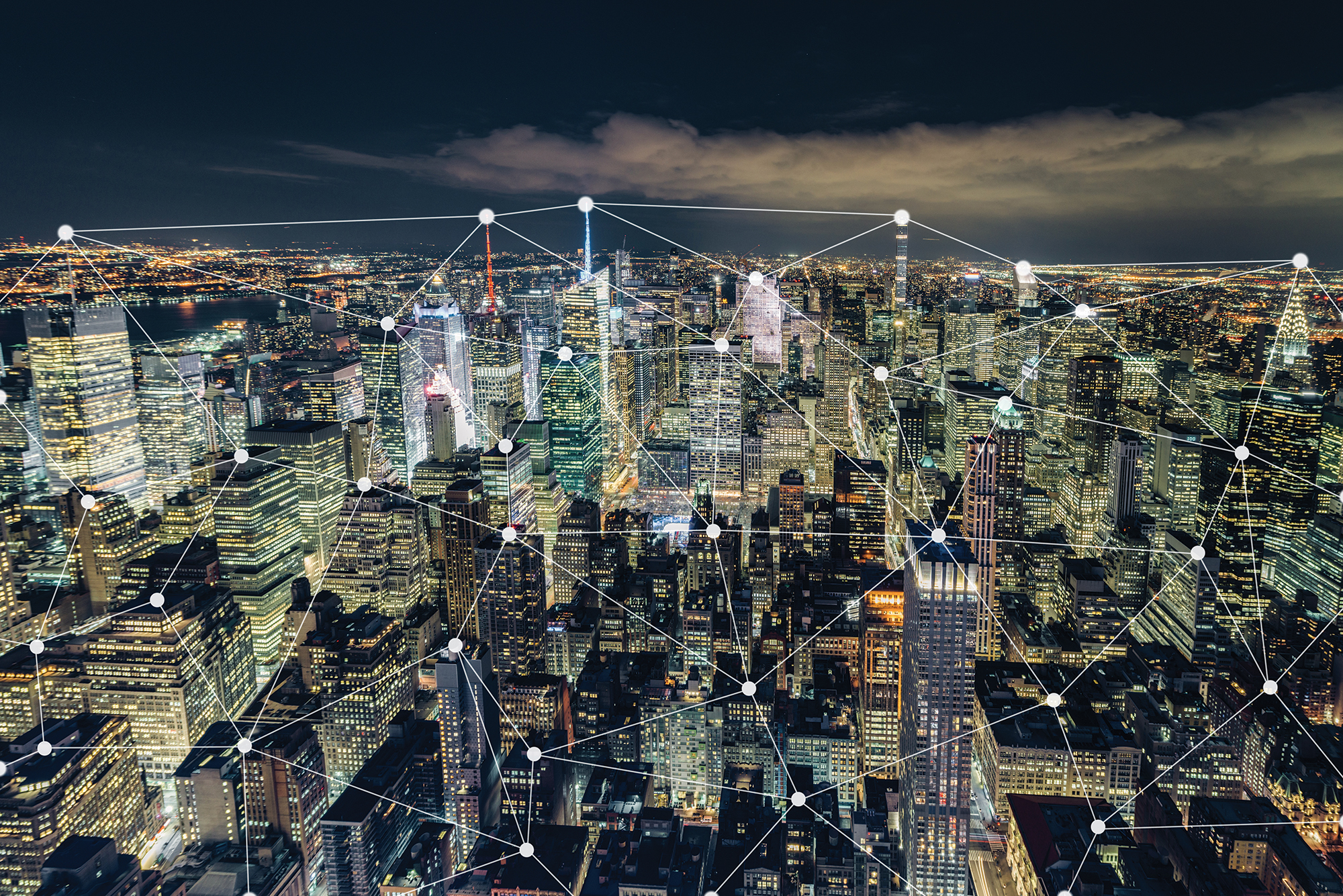 New York City skyline at night with illuminated skyscrapers, overlaid with a digital network grid of interconnected nodes, symbolizing connectivity and smart city technology.
