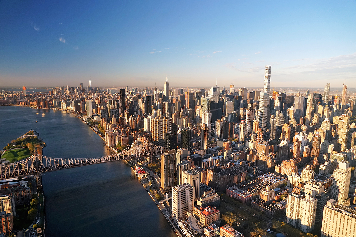 Aerial view of Manhattan, New York City, with the Queensboro Bridge spanning the East River and numerous skyscrapers rising under a clear blue sky. Photo by Jerry Trudell.