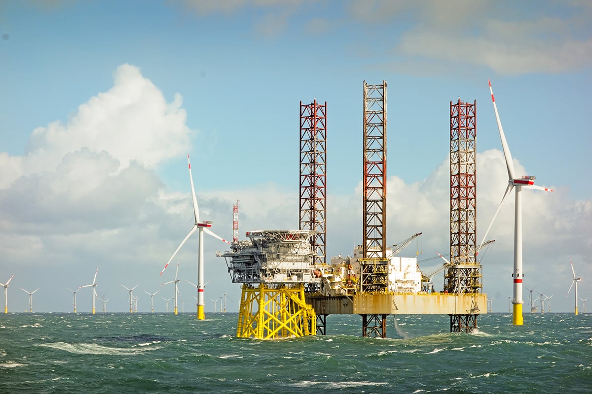 Large offshore 8MW wind turbines, wind farm on the horizon in north sea with jack up boat and offshore platform in wavy sea
