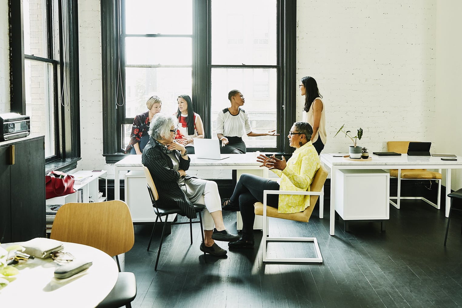 Six female coworkers in discussion during team meeting in creative office.