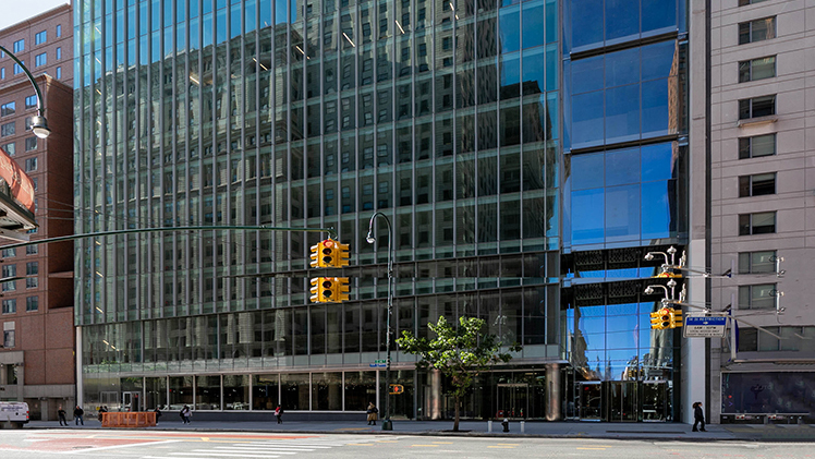 Modern glass office building named Civic Hall with reflections of nearby structures, sidewalk, and traffic lights on a sunny day in Union Square.