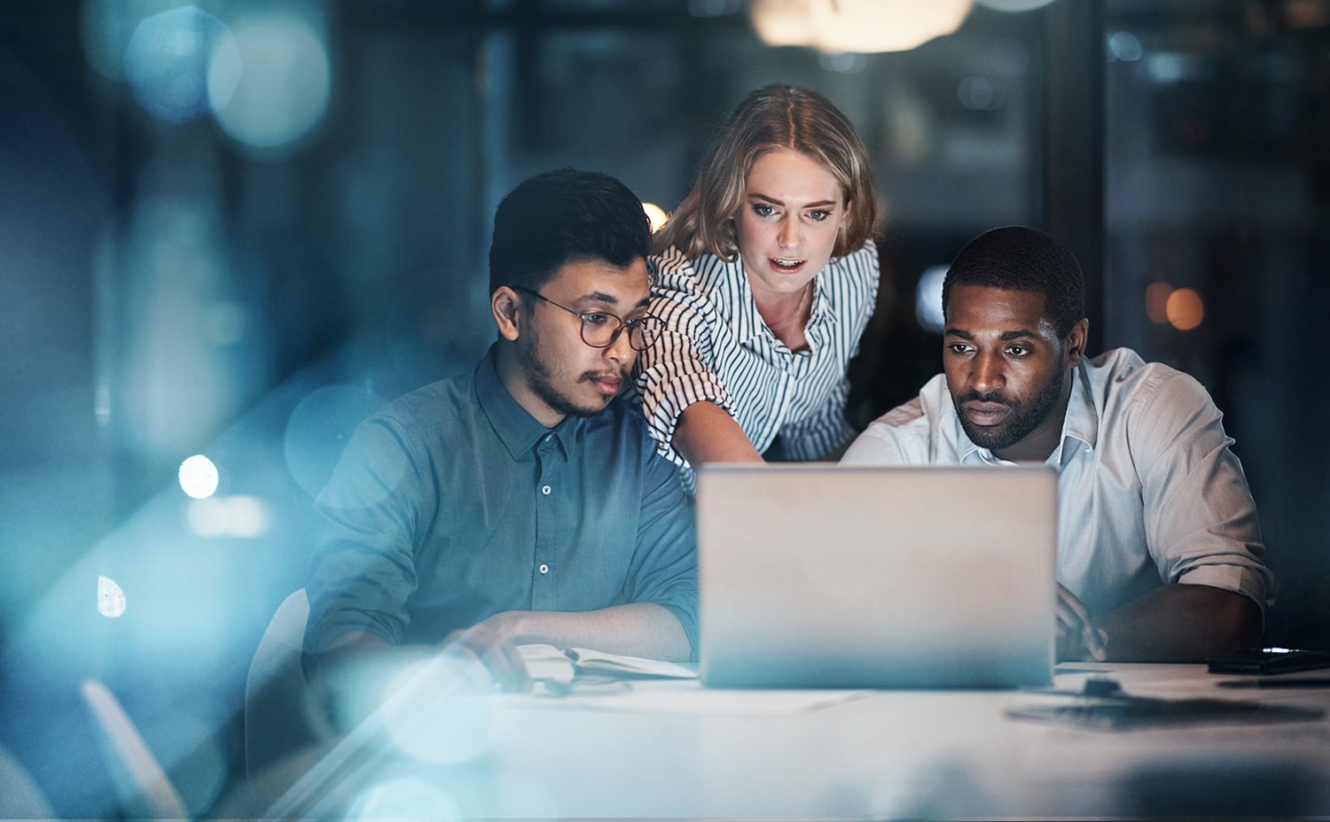 Three young businesspeople working together on a laptop in their office late at night.