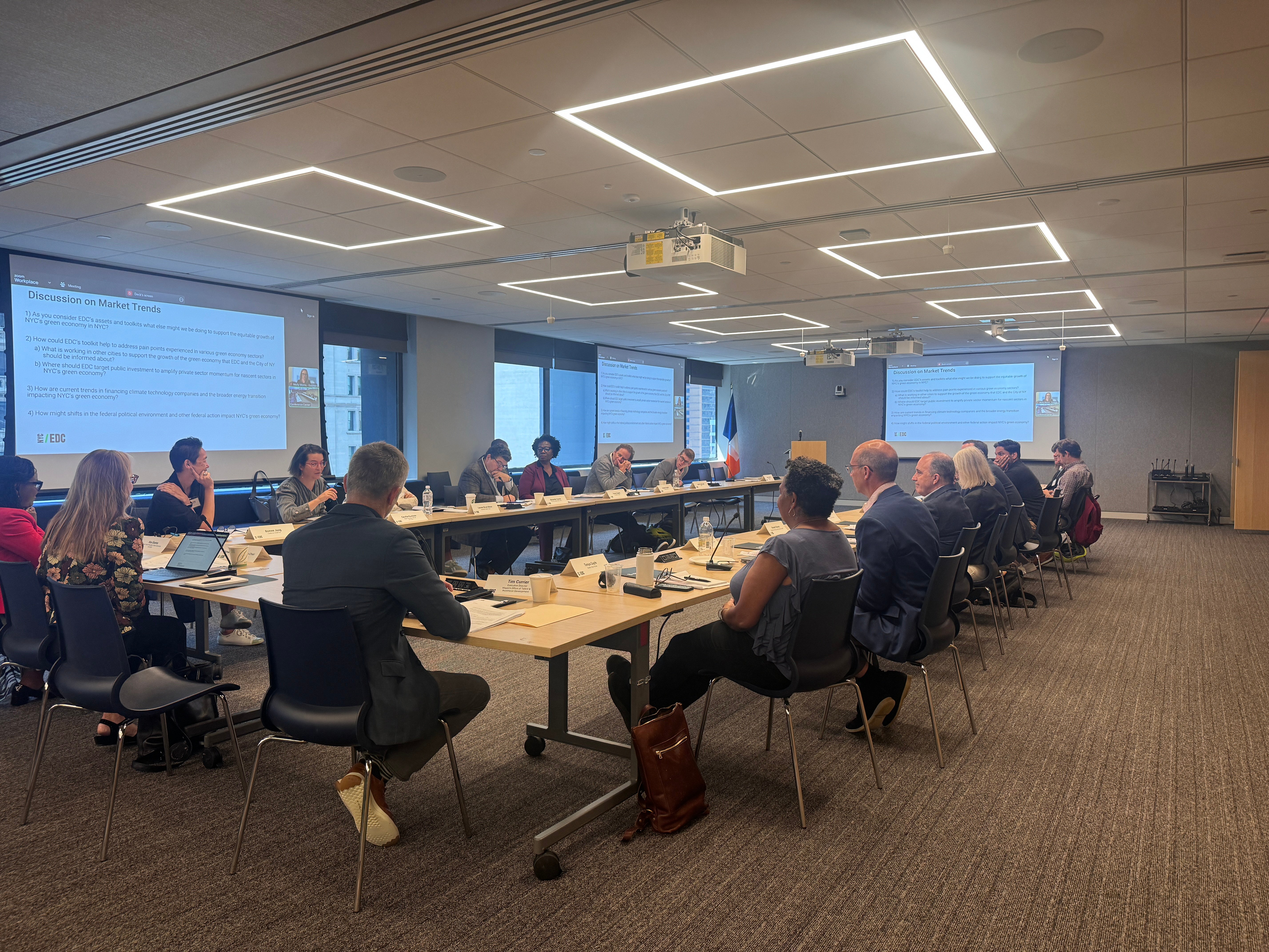 New York City Economic Development Corporation Green Economy Advisory Council members sit around a large conference table in a meeting room with presentations displayed on screens at both ends.
