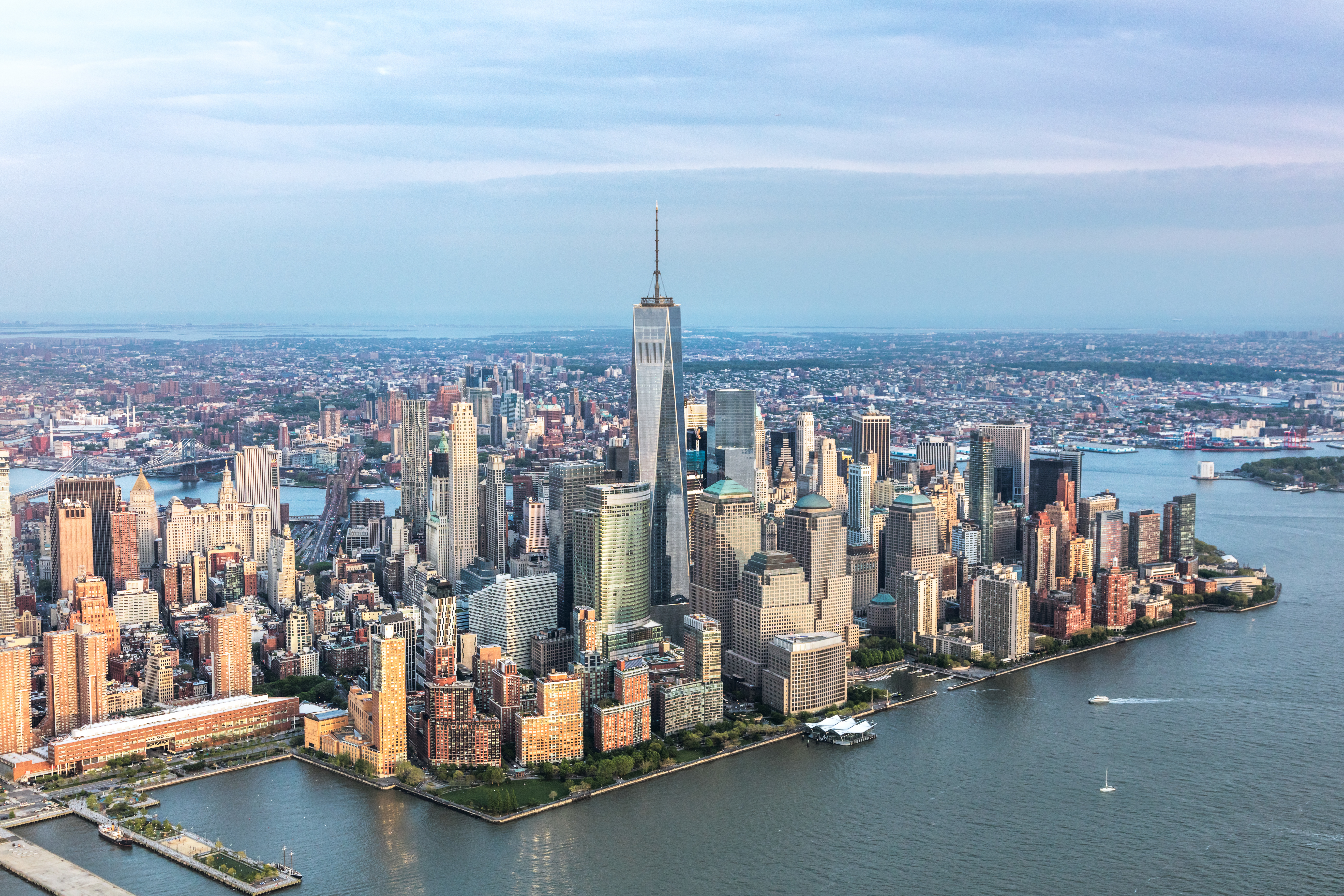Aerial view of a downtown Manhattan skyline with tall buildings and skyscrapers, surrounded by water, under a cloudy sky.