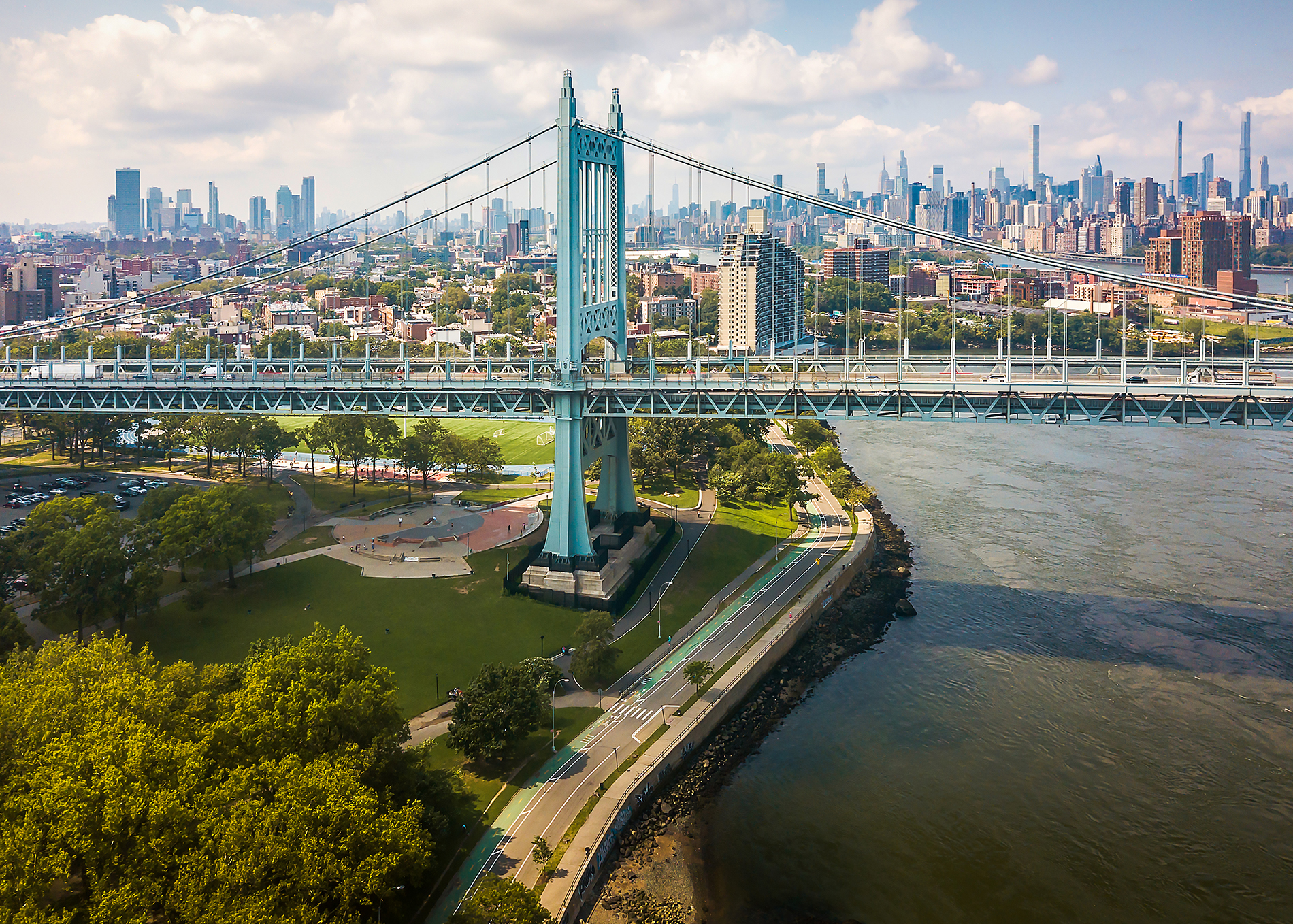 Aerial view of the Robert F. Kennedy Bridge (formerly Triborough Bridge) spanning over water, with Manhattan’s skyline in the background and green parks and roads visible below.