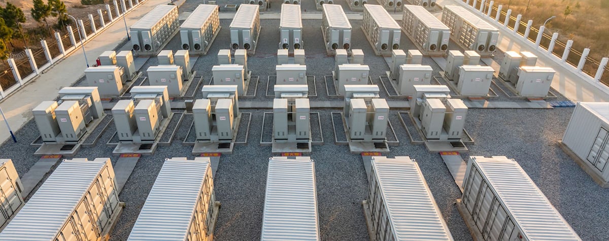 Aerial view of a large battery energy storage power station with rows of white storage containers and electrical equipment on a gravel lot, arranged in an organized grid pattern.