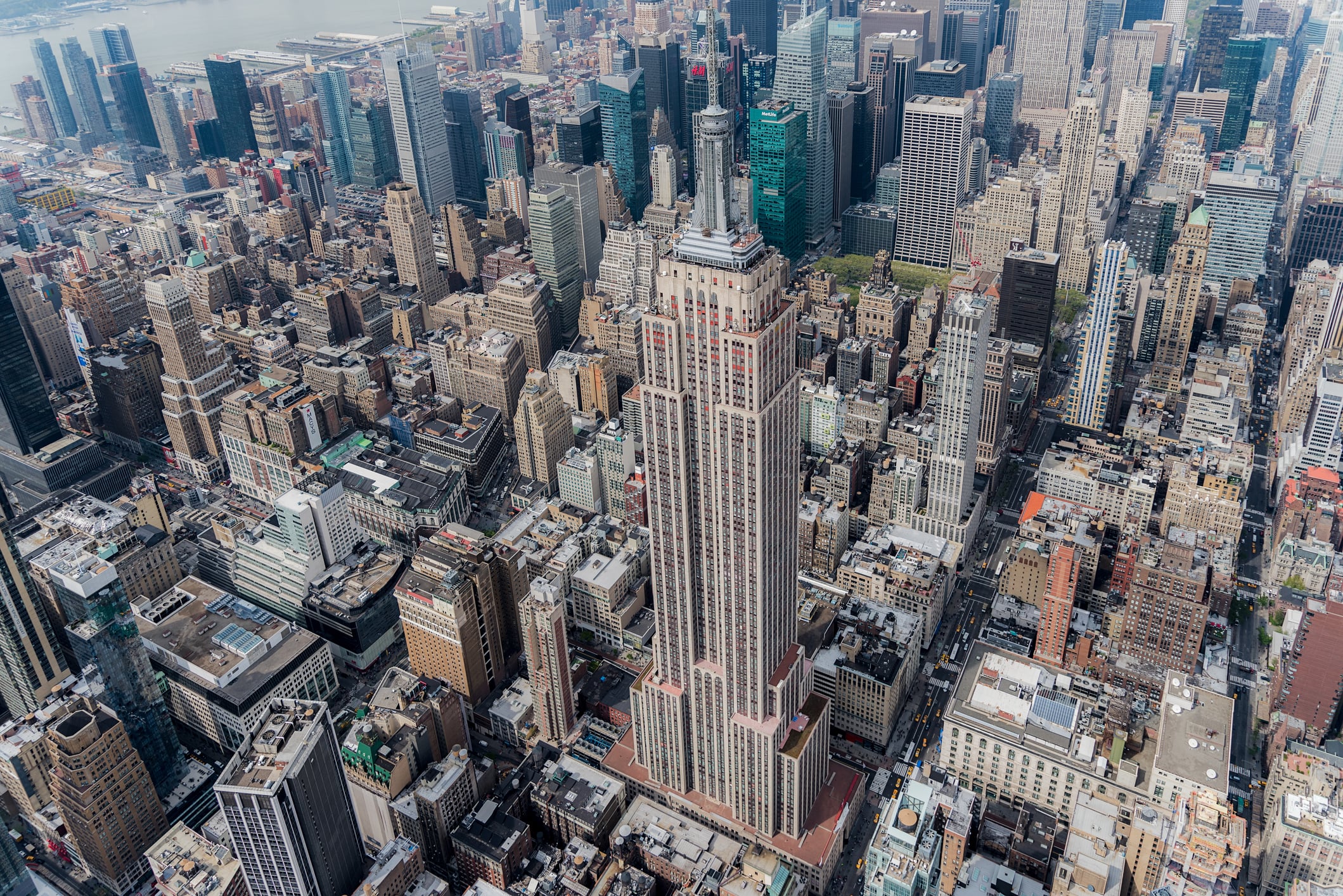 Aerial view of the Empire State Building surrounded by densely packed skyscrapers and New York City streets in Midtown Manhattan on a clear day.