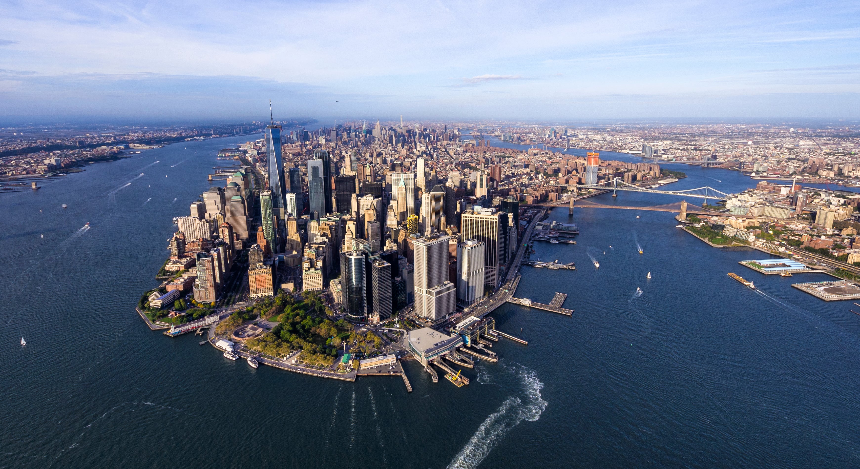 Aerial view of Lower Manhattan, New York City, showing skyscrapers, waterfront parks, and surrounding rivers with boats. The Brooklyn and Manhattan bridges are visible in the background. Photo by Eloi Omella/Getty Images.