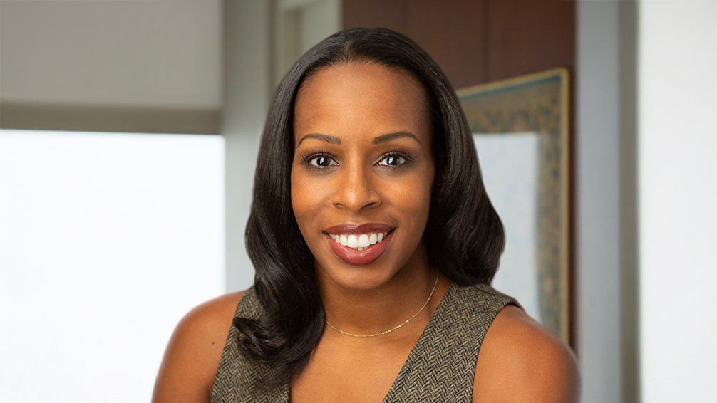 Headshot of Margaret Anadu shows a woman with long, dark hair and a nose piercing smiles at the camera. She is wearing a sleeveless brown top and a thin gold necklace, standing in an indoor setting with neutral-toned walls.