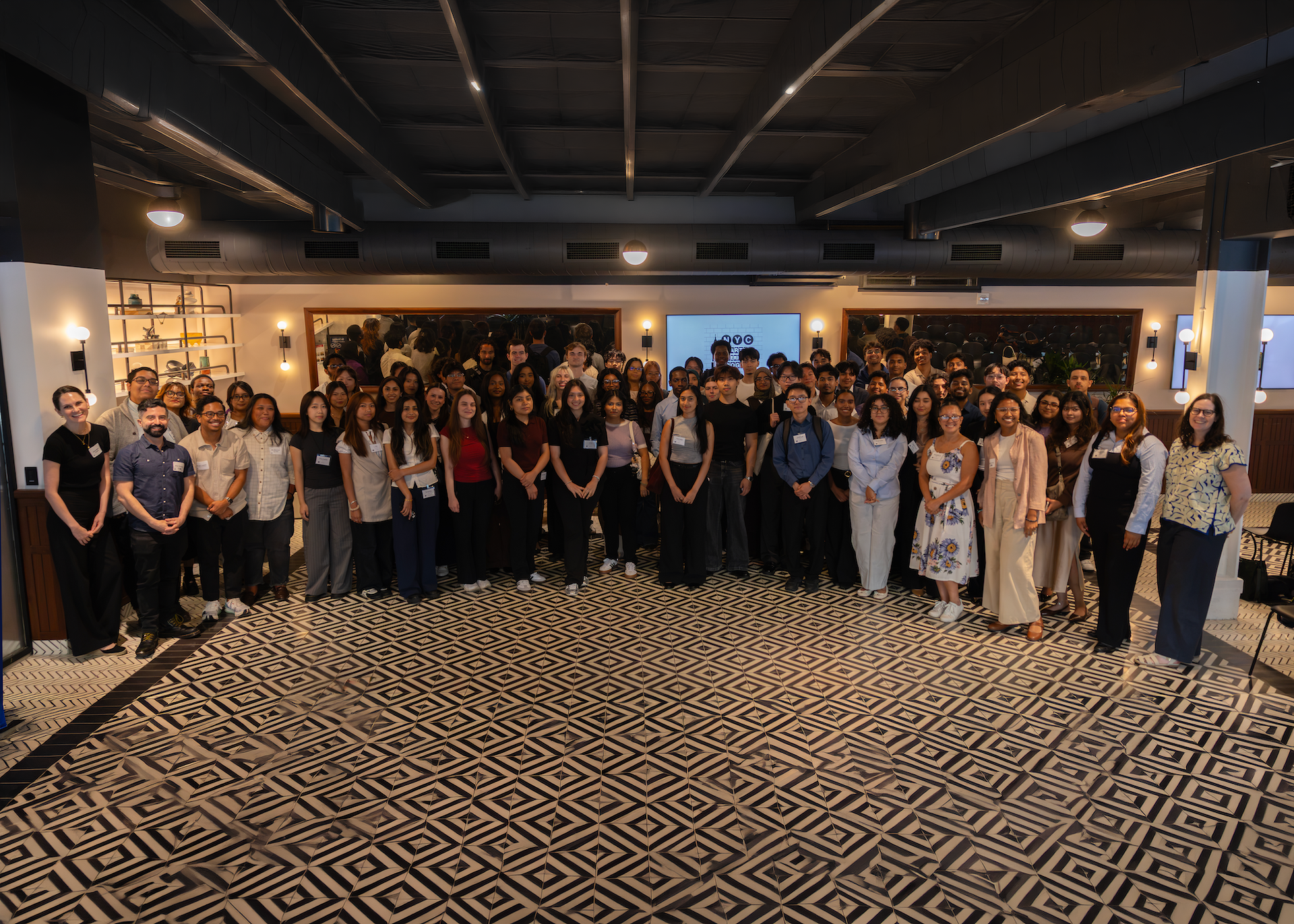 Startup and Venture Capital 2026 intern cohort pose for a photo in a spacious, modern room with patterned flooring, ceiling lights, and shelves in the background.