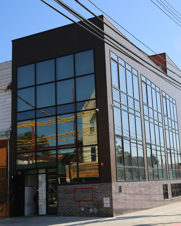 A modern, three-story building with large glass windows and a brick base, reflecting nearby structures and power lines under a clear blue sky.