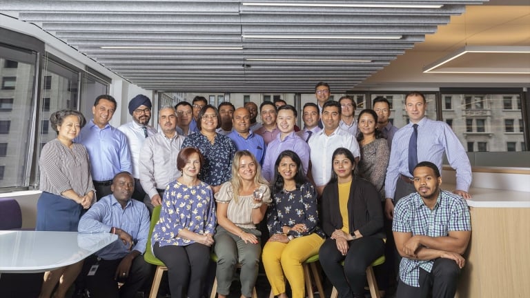 A diverse group of twenty-two people, both seated and standing, pose for a professional photo in an office setting. They are dressed in business attire, and the background features large windows with a city view. A diverse group of twenty-two people, both seated and standing, pose for a professional photo in an office setting. They are dressed in business attire, and the background features large windows with a city view.