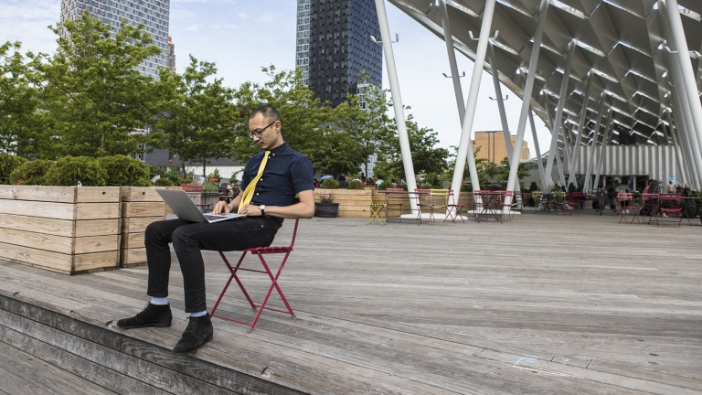 Businessman typing on laptop outside hotel.