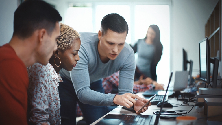 Closeup side view of group of mid 20&#039;s mobile application developers testing the code and fixing the issues.