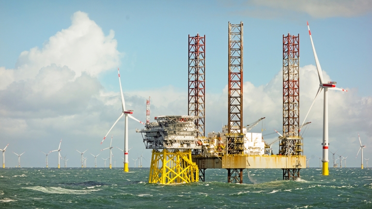 Large offshore 8MW wind turbines, wind farm on the horizon in north sea with jack up boat and offshore platform in wavy sea