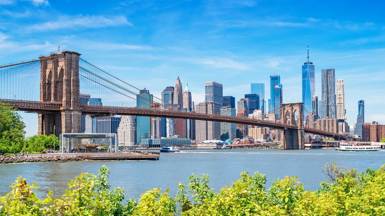 The Brooklyn Bridge and the skyline of New York City USA as seen form Brooklyn, across the East River, on a sunny summer day.