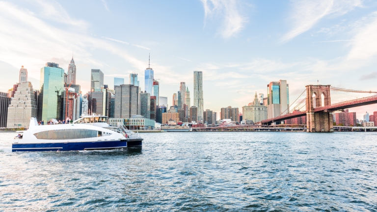 View of NYC Ferry with Lower Manhattan skyline and Brooklyn Bridge in the background at sunset
