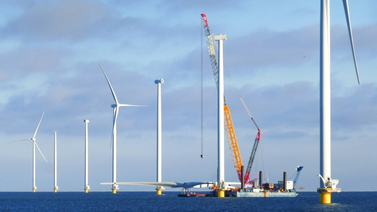 Construction of offshore wind farm. Crane ship is preparing for lifting up rotor of the wind turbine.