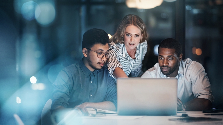 Three young business people working together on a laptop in their office late at night.