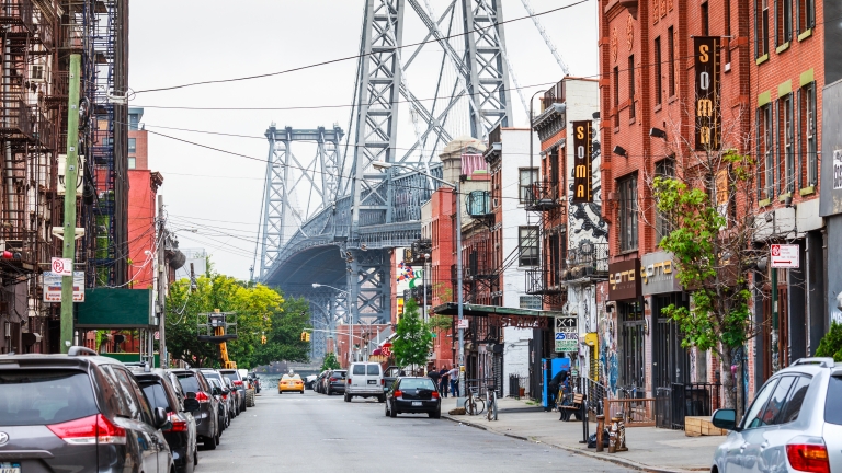 Street lined with shops with Williamsburg Bridge in the background.