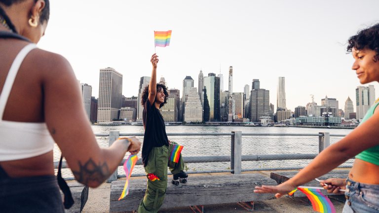 Group of roller skate dancers training and performing outdoors with rainbow flags in front of the view of Manhattan from the Brooklyn Heights.