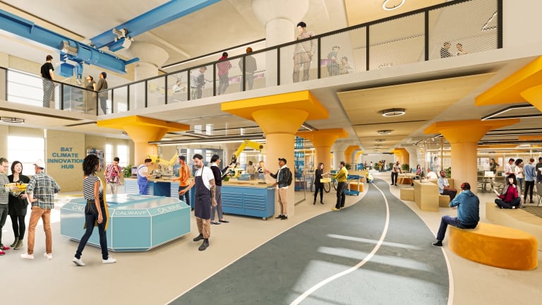 People interacting, working, and relaxing at Brooklyn Army Terminal, a large and modern indoor space. Features include workstations, seating areas, and upper-level walkways, all with bright yellow structural columns and accents.