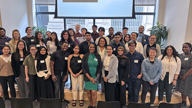 A group of summer interns pose for a photo in front of a screen displaying &quot;Blackstone LaunchPad.&quot; They are in an indoor setting with windows and plants in the background.