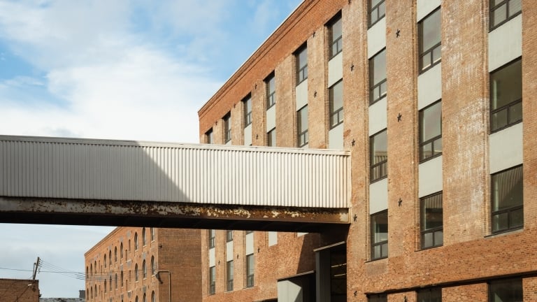 A brick MiNY building with large windows connected by an elevated walkway, under a blue sky with clouds.