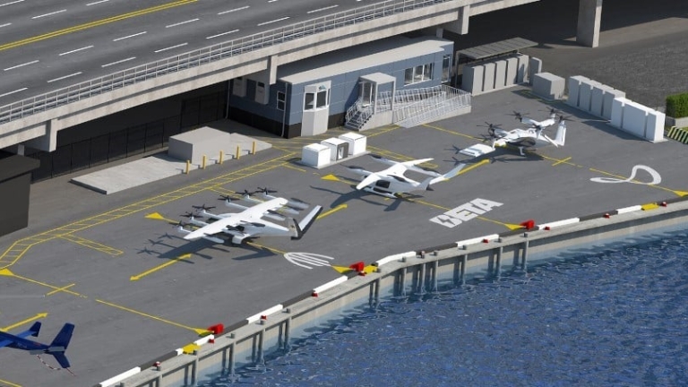 Aerial view of the urban 34th Street Heliport with multiple white eVTOL aircraft parked on marked spots near a modern building, adjacent to a bridge over the waterfront.