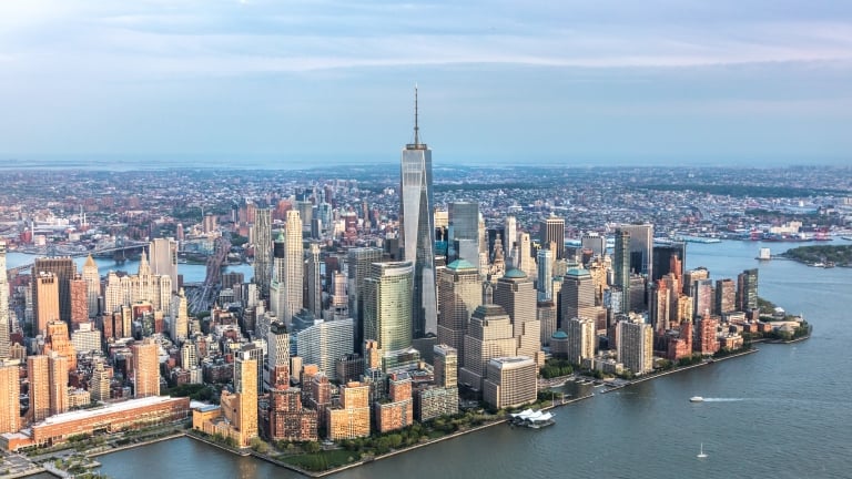 Aerial view of a downtown Manhattan skyline with tall buildings and skyscrapers, surrounded by water, under a cloudy sky.