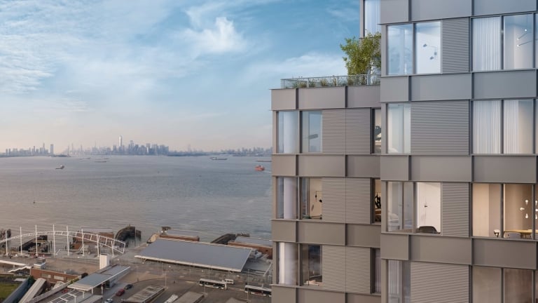 A modern high-rise building with large windows, overlooks a waterfront, with boats on the water and a New York City skyline visible in the distance under a blue sky. A modern high-rise building with large windows, overlooks a waterfront, with boats on the water and a New York City skyline visible in the distance under a blue sky.