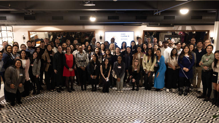 Members of the large, diverse 2025 Founder Fellowship cohort pose and smile for a group photo in a well-lit indoor space with patterned flooring.