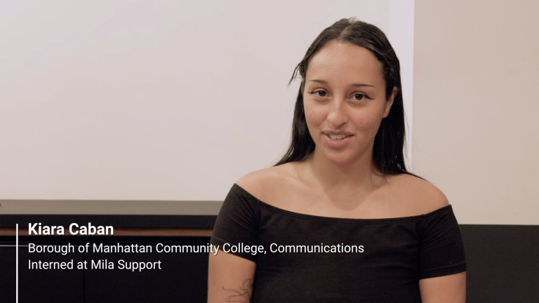 A woman with long dark hair, wearing an off-the-shoulder black top, sits and smiles at the camera. On-screen text reads: Kiara Caban, Borough of Manhattan Community College, Communications. Interned at Mila Support.