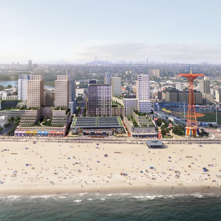 Aerial view of a beach with people, adjacent buildings, and a ferris wheel-like structure in an urban setting.