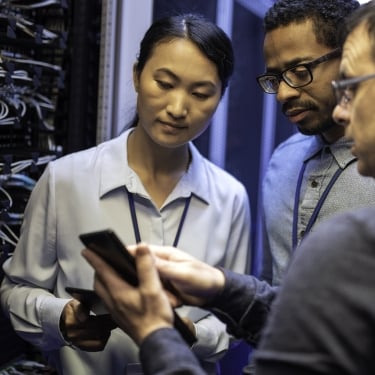 Three IT technician looking at a digital tablet and talking while standing next to a server in a data center