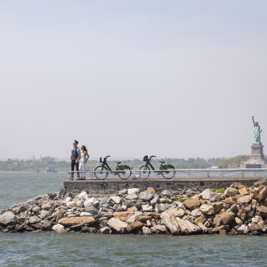 Couple standing on observation point with Statue of Liberty in background against clear sky.