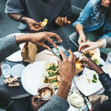 A multi-ethnic group of friends enjoy tacos and chips at a Mexican food cart in downtown New York City, New York. They laugh and talk while eating their food, having fun sharing life and culture. One of them takes a picture of their food with his smartphone to share on his social networks. A multi-ethnic group of friends enjoy tacos and chips at a Mexican food cart in downtown New York City, New York. They laugh and talk while eating their food, having fun sharing life and culture. One of them takes a picture of their food with his smartphone to share on his social networks.