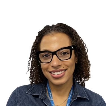 Katia Barnave wearing glasses, a dark denim shirt, and a blue lanyard. She is smiling against a plain white background.