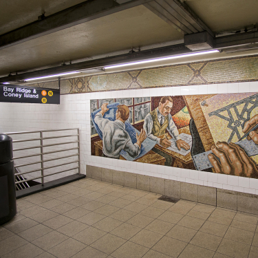 Mural in a subway station shows two men at a desk examining maps and architectural plans. Hands and tools are visible. Above, a sign indicates directions to Bay Ridge and Coney Island. The area is lit with overhead fluorescent lights.