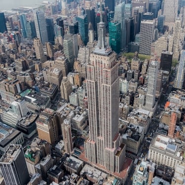 Aerial view of the Empire State Building surrounded by densely packed skyscrapers and New York City streets in Midtown Manhattan on a clear day.