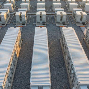 Aerial view of a grid of large, rectangular industrial containers and units arranged on a gravel lot, part of a battery storage facility.