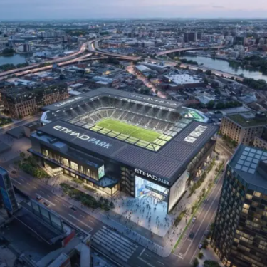 Aerial rendering of a modern, illuminated stadium named Etihad Park filled with a crowd, in Willets Point, Queens. It is surrounded by buildings, roads, and a river in the background at dusk.