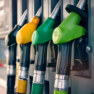 Close-up of four fuel pump nozzles at a gas station, with different colored handles including yellow, green, and black, indicating different fuel types. The nozzles are attached to the fuel dispenser.
