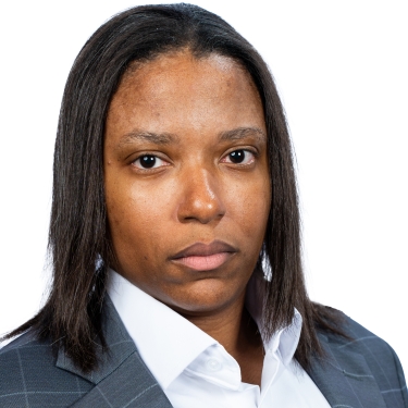 Antoya Debarros with straight, shoulder-length hair wearing a gray plaid suit jacket and a white collared shirt poses against a plain white background with a serious expression.