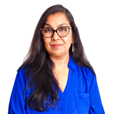 Jyoti Jaiswal with long dark hair and glasses wearing a bright blue shirt stands against a plain light background, looking at the camera with a neutral expression.