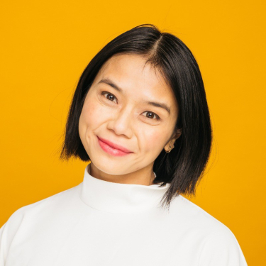 Mai-Truong smiles at the camera against a yellow background.
