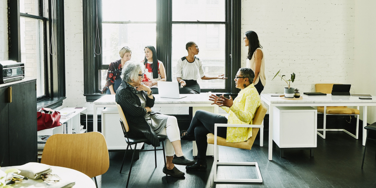 Six female coworkers in discussion during team meeting in creative office.