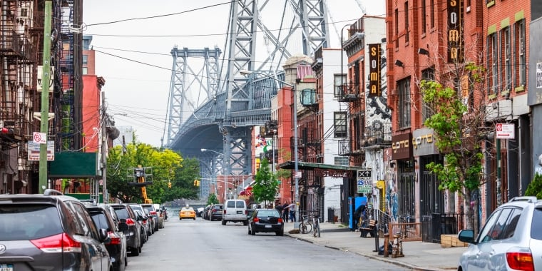 Street lined with shops with Williamsburg Bridge in the background.