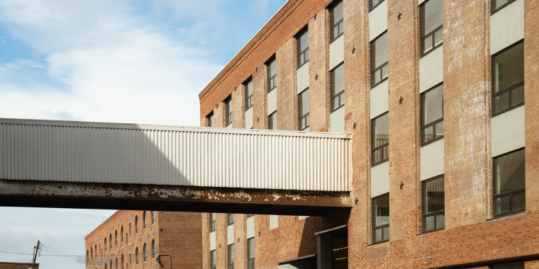 A brick MADE building with large windows connected by an elevated walkway, under a blue sky with clouds.